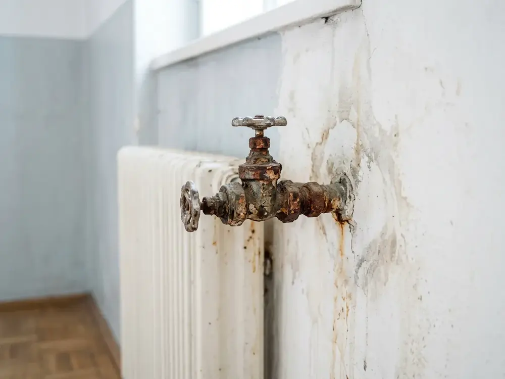 Rostiges Heizkörperventil mit Verfärbung an der Wand