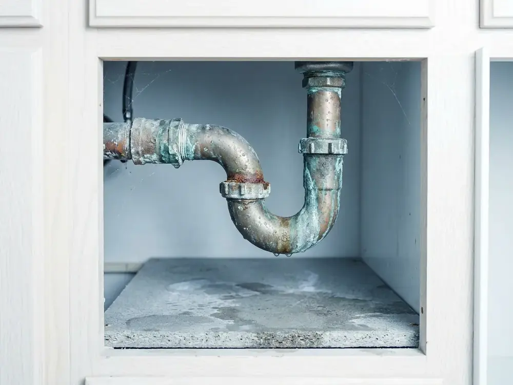 Korrodierter Siphon unter dem Waschbecken mit feuchtem Schrankboden